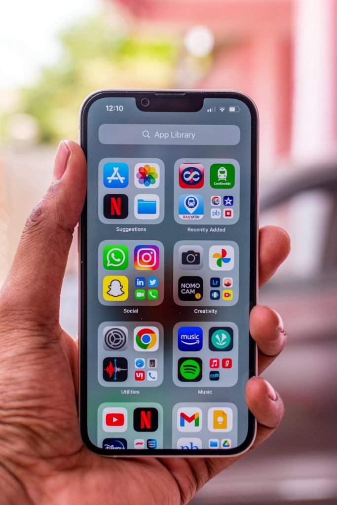 Close-up of hand holding a smartphone with various app icons on the screen outdoors.